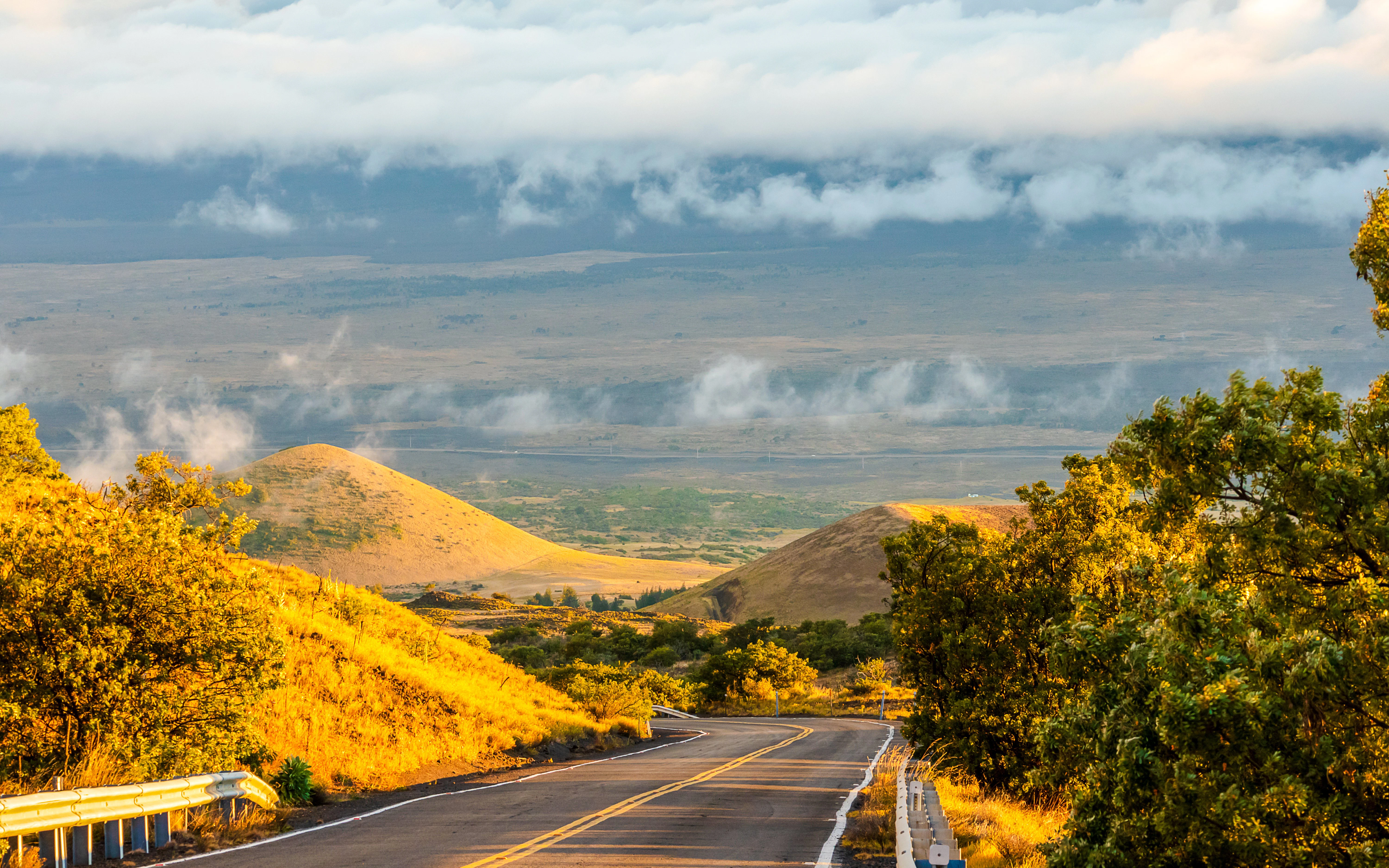 Road leading to Mauna Kea observatories with scenic sunset and rolling hills.