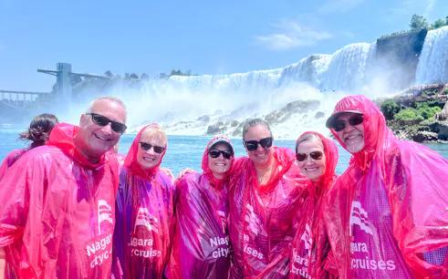 Visitors in red ponchos on a Niagara Falls boat tour with the waterfall in the background.
