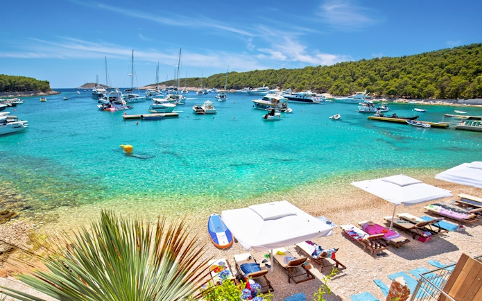 Yachts anchored at Palmizana turquoise beach, Pakleni Otoci islands, with sun loungers and umbrellas.