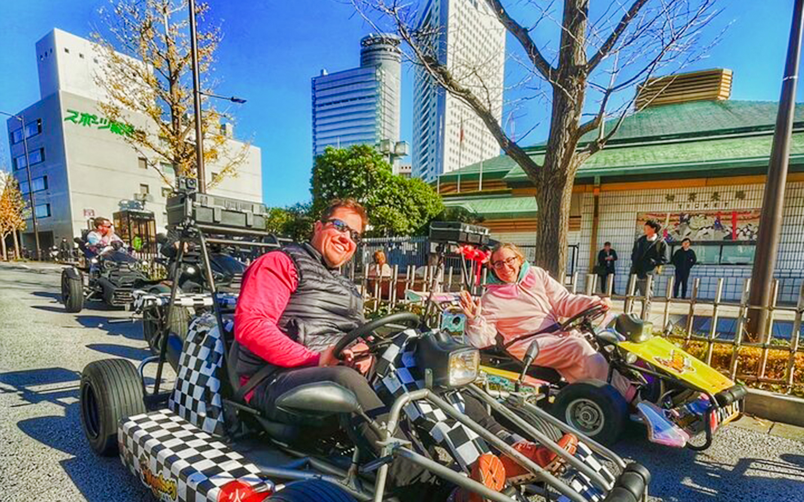 Two people riding go-karts on a Tokyo street with city buildings in the background.