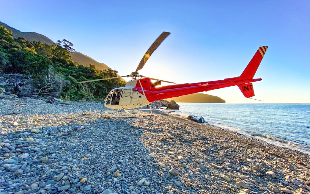 Red and white helicopter on a remote beach near Milford Sound, New Zealand, during a Queenstown tour.