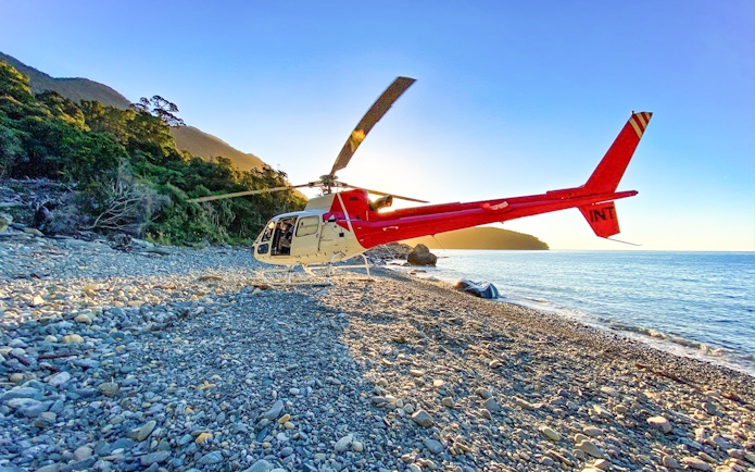 Red and white helicopter on a remote beach near Milford Sound, New Zealand, during a Queenstown tour.