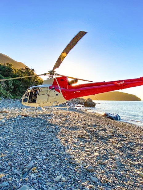Red and white helicopter on a remote beach near Milford Sound, New Zealand, during a Queenstown tour.