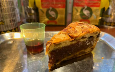 Pastry slice with almonds and a small cup of liqueur on a tray during The Hague food tour.