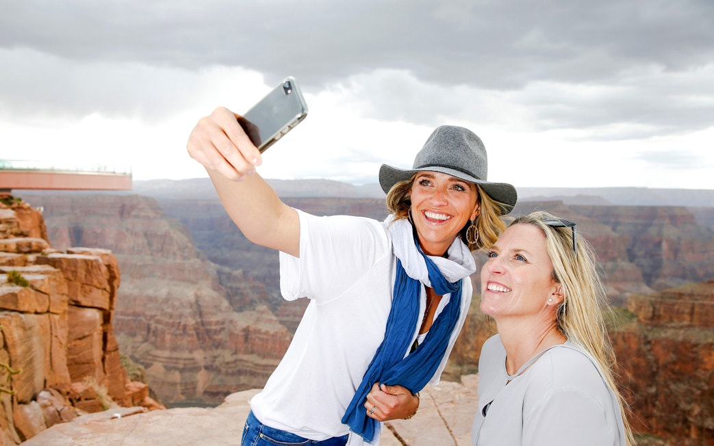 Two women taking a selfie at the Grand Canyon Skywalk with canyon view.