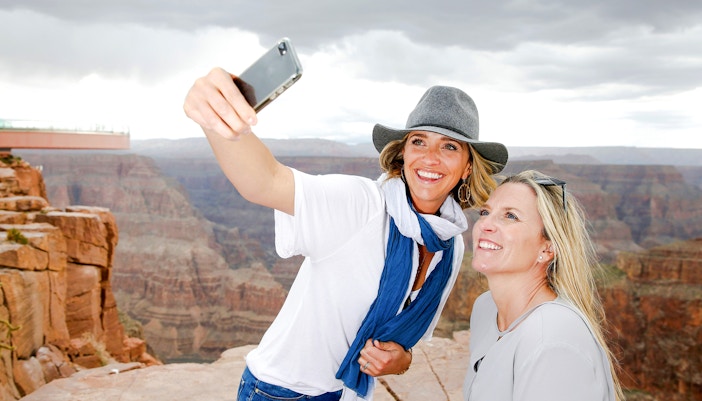 Two women taking a selfie at the Grand Canyon Skywalk with canyon view.