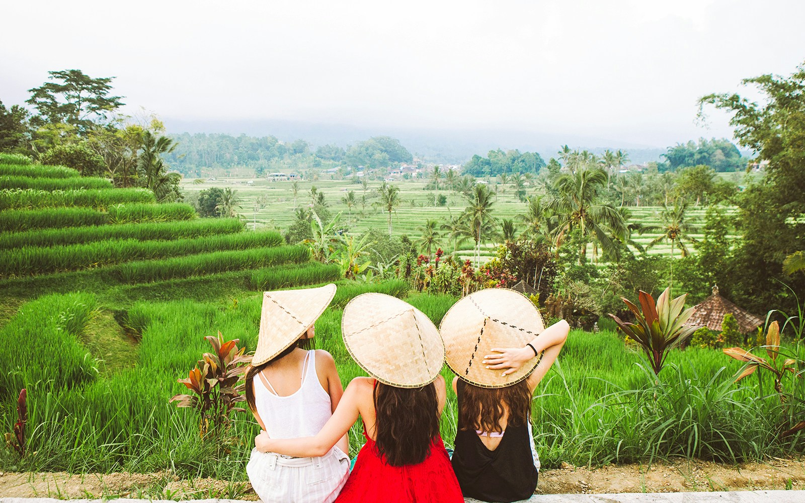 Three people in traditional hats overlooking rice terraces in Ubud, Bali.