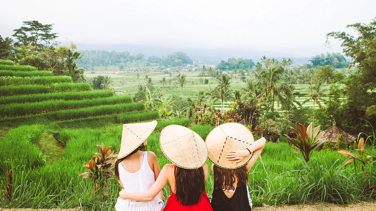 Three people in traditional hats overlooking rice terraces in Ubud, Bali.