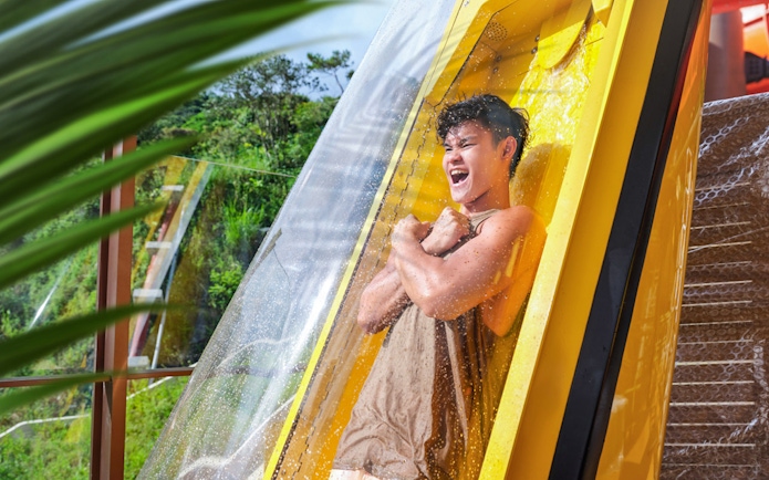 Person enjoying a water slide at Ocean Park with lush greenery in the background.