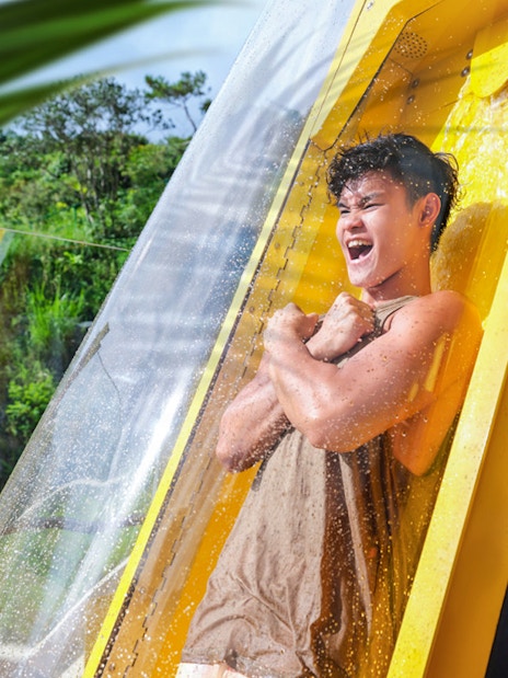 Person enjoying a water slide at Ocean Park with lush greenery in the background.