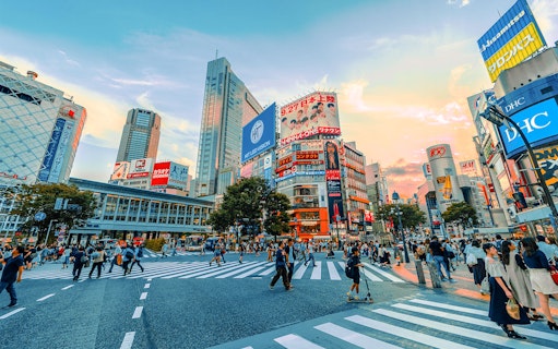 Shibuya Crossing bustling with people, surrounded by vibrant billboards during a Japanese street food tour.