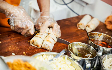 Chef slicing spring rolls on a food tour with sauces and ingredients nearby.