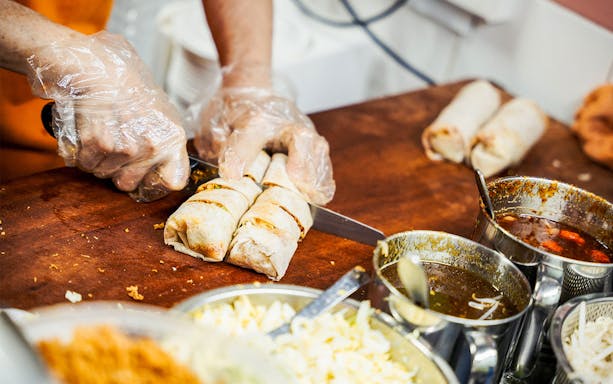 Chef slicing spring rolls on a food tour with sauces and ingredients nearby.