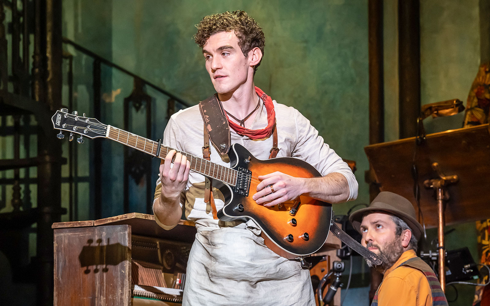 Musician playing guitar on stage during Hadestown musical performance.