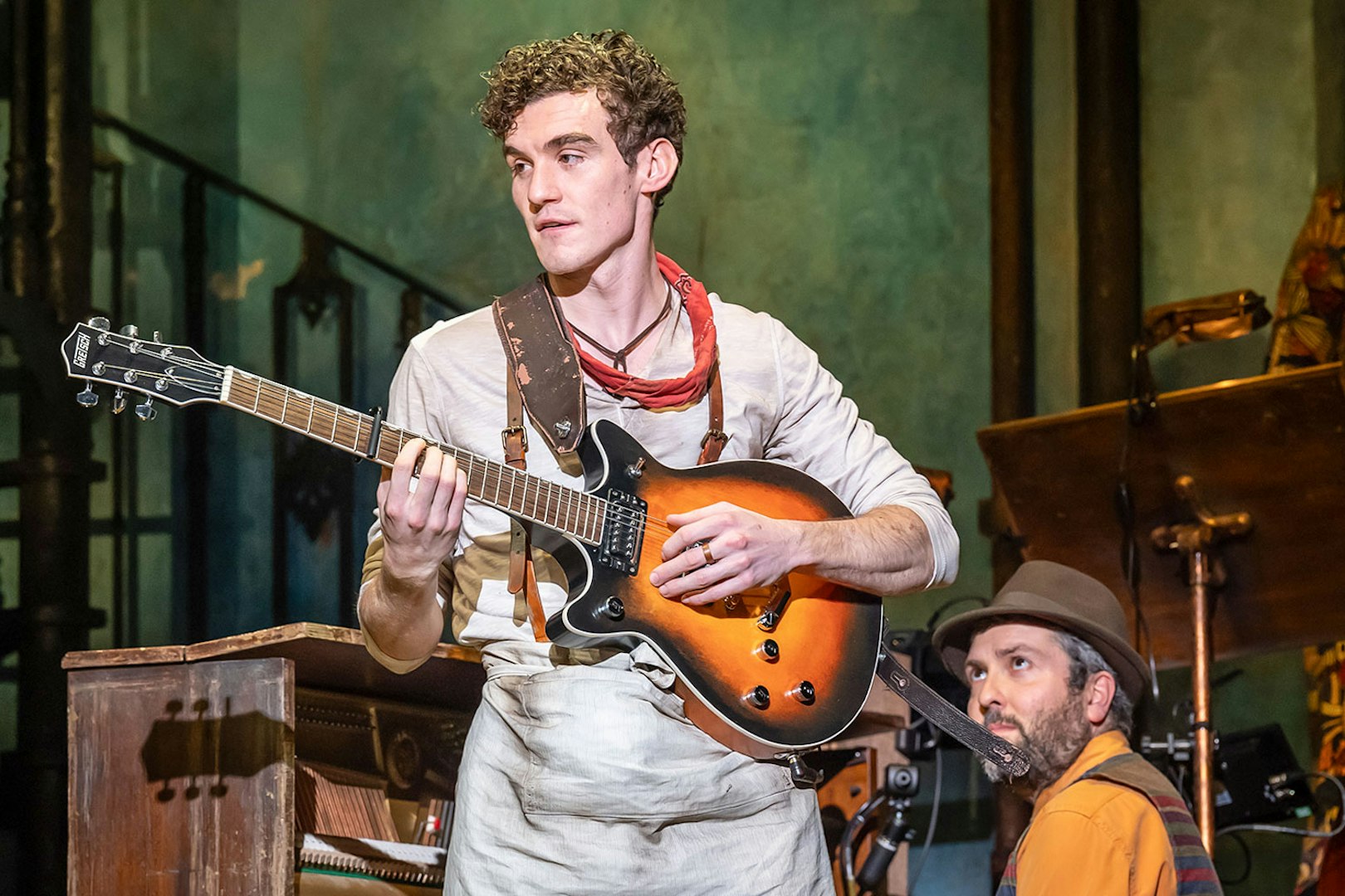 Musician playing guitar on stage during Hadestown musical performance.