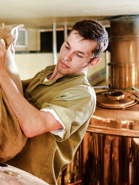 Man handling grain sack in brewery setting.