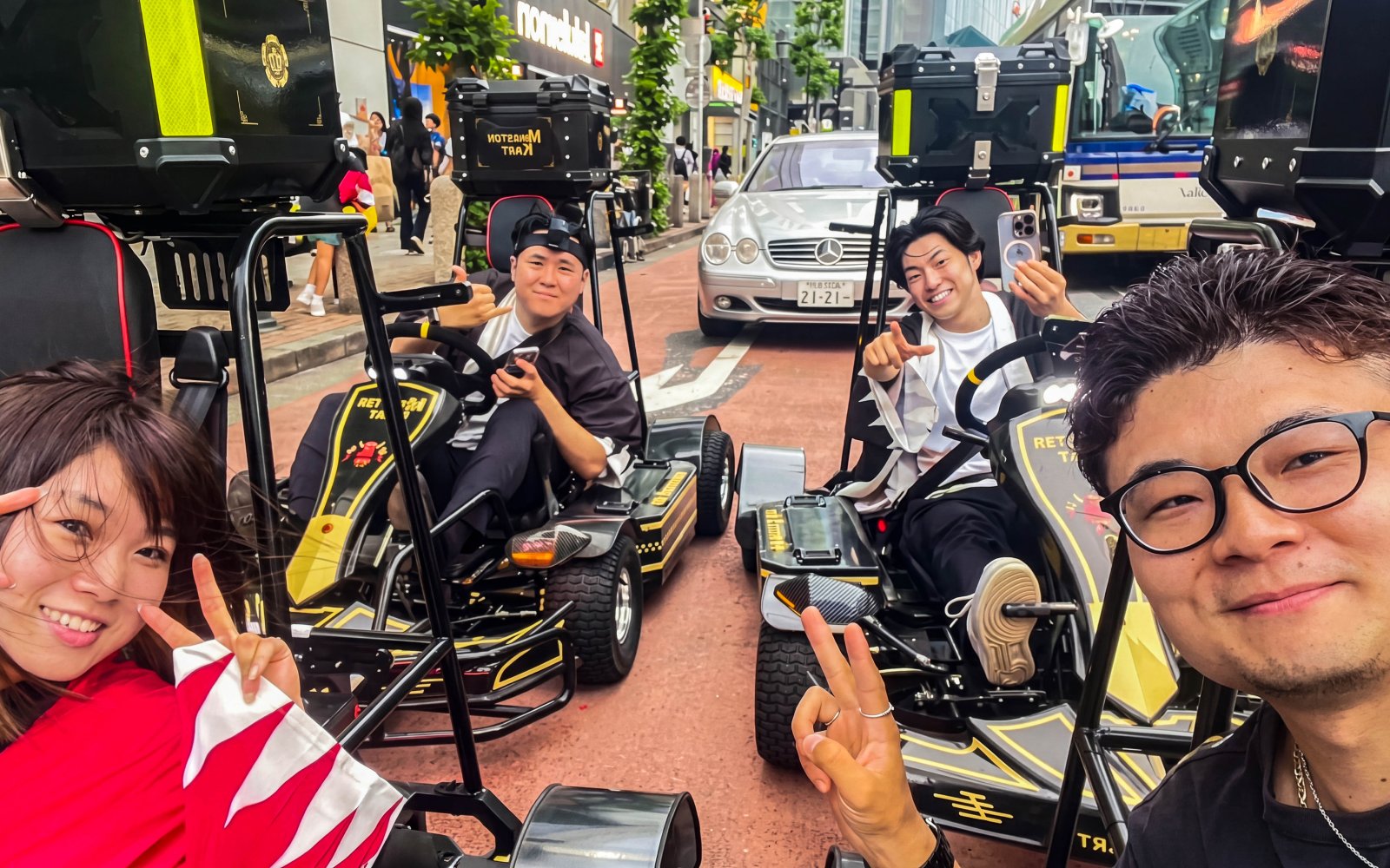 People enjoying a street kart experience in Tokyo, posing with peace signs on a busy city street.