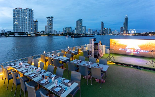 Dinner setup on a cruise ship deck with Chao Phraya River and Bangkok skyline in the background.