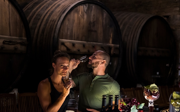 Wine tasting in a Porto cellar with large wooden barrels in the background.