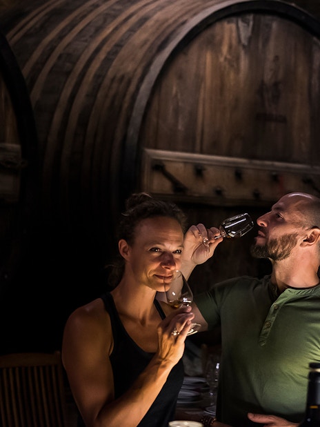 Wine tasting in a Porto cellar with large wooden barrels in the background.