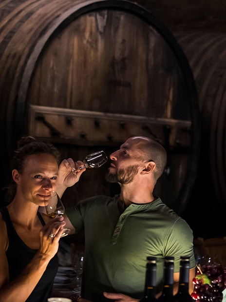 Wine tasting in a Porto cellar with large wooden barrels in the background.