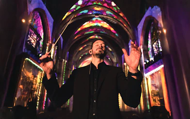 Conductor leading a performance under colorful lights at Westminster Cathedral, London.
