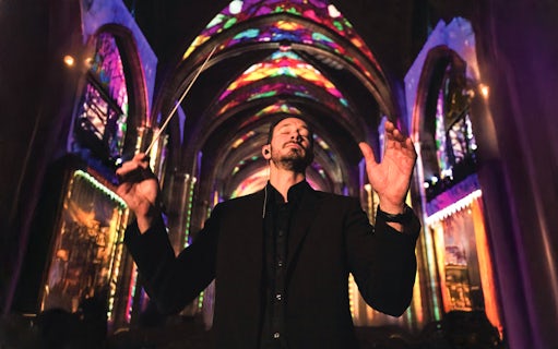 Conductor leading a performance under colorful lights at Westminster Cathedral, London.