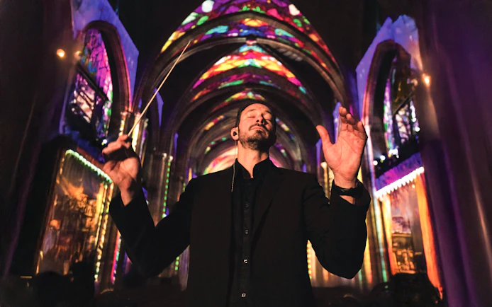 Conductor leading a performance under colorful lights at Westminster Cathedral, London.