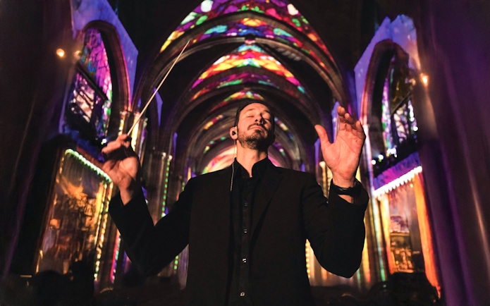 Conductor leading a performance under colorful lights at Westminster Cathedral, London.