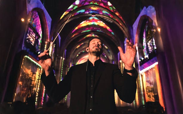Conductor leading a performance under colorful lights at Westminster Cathedral, London.
