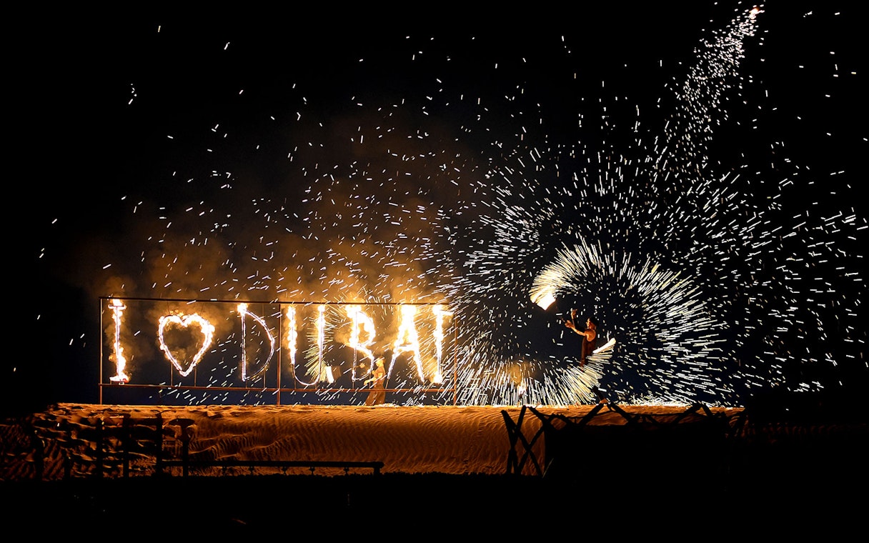 Fire performer with "I ♥ DUBAI" sign during evening desert safari.