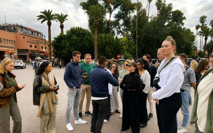 Tour group in Marrakech Medina with guide, surrounded by palm trees and traditional buildings.