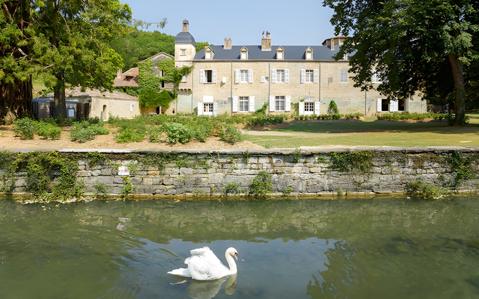 Swan swimming in front of Beaulieu-en-Rouergue Abbey, France.