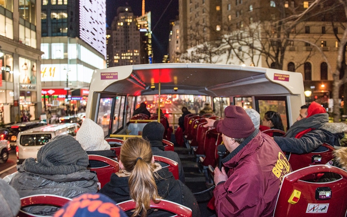 Passengers on a Big Bus night tour in New York City, viewing illuminated skyscrapers.