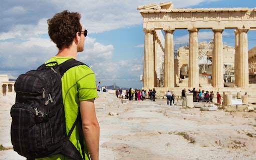 Tourist with backpack viewing the Parthenon at the Acropolis, Athens.
