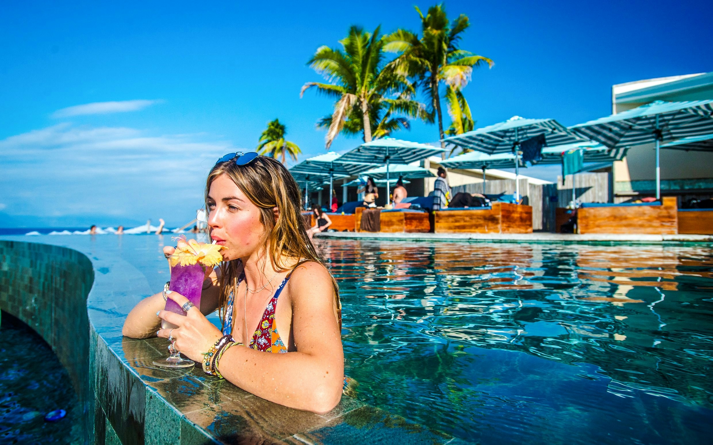 Woman sipping a drink in the pool at Malamala Beach Club, Fiji, with palm trees in the background.
