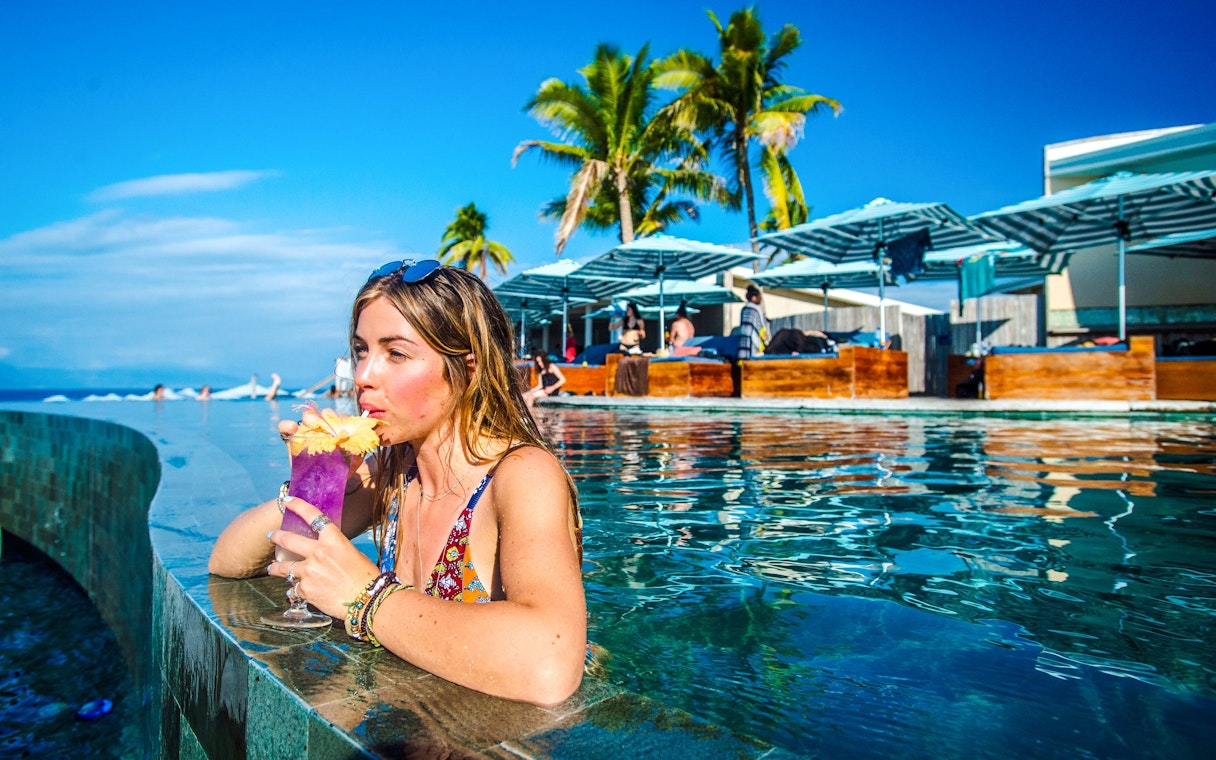 Woman sipping a drink in the pool at Malamala Beach Club, Fiji, with palm trees in the background.