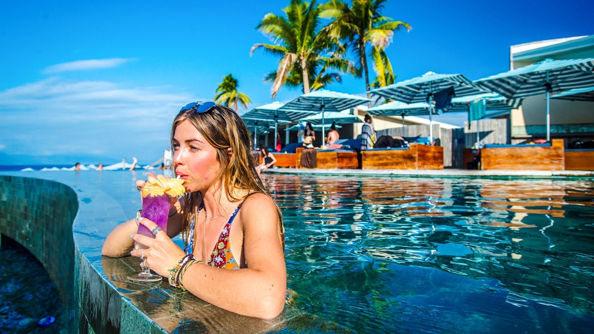 Woman sipping a drink in the pool at Malamala Beach Club, Fiji, with palm trees in the background.