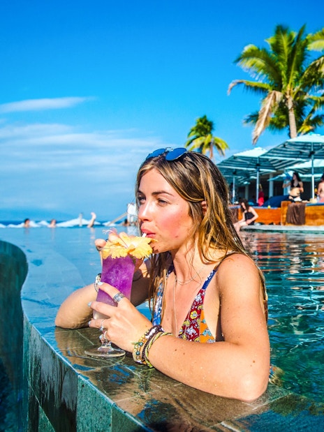 Woman sipping a drink in the pool at Malamala Beach Club, Fiji, with palm trees in the background.