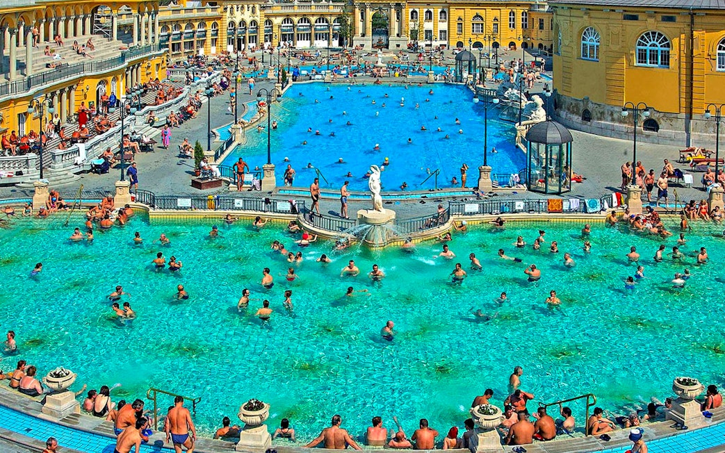 Outdoor pool at Széchenyi Thermal Bath, Budapest, with people swimming and relaxing.