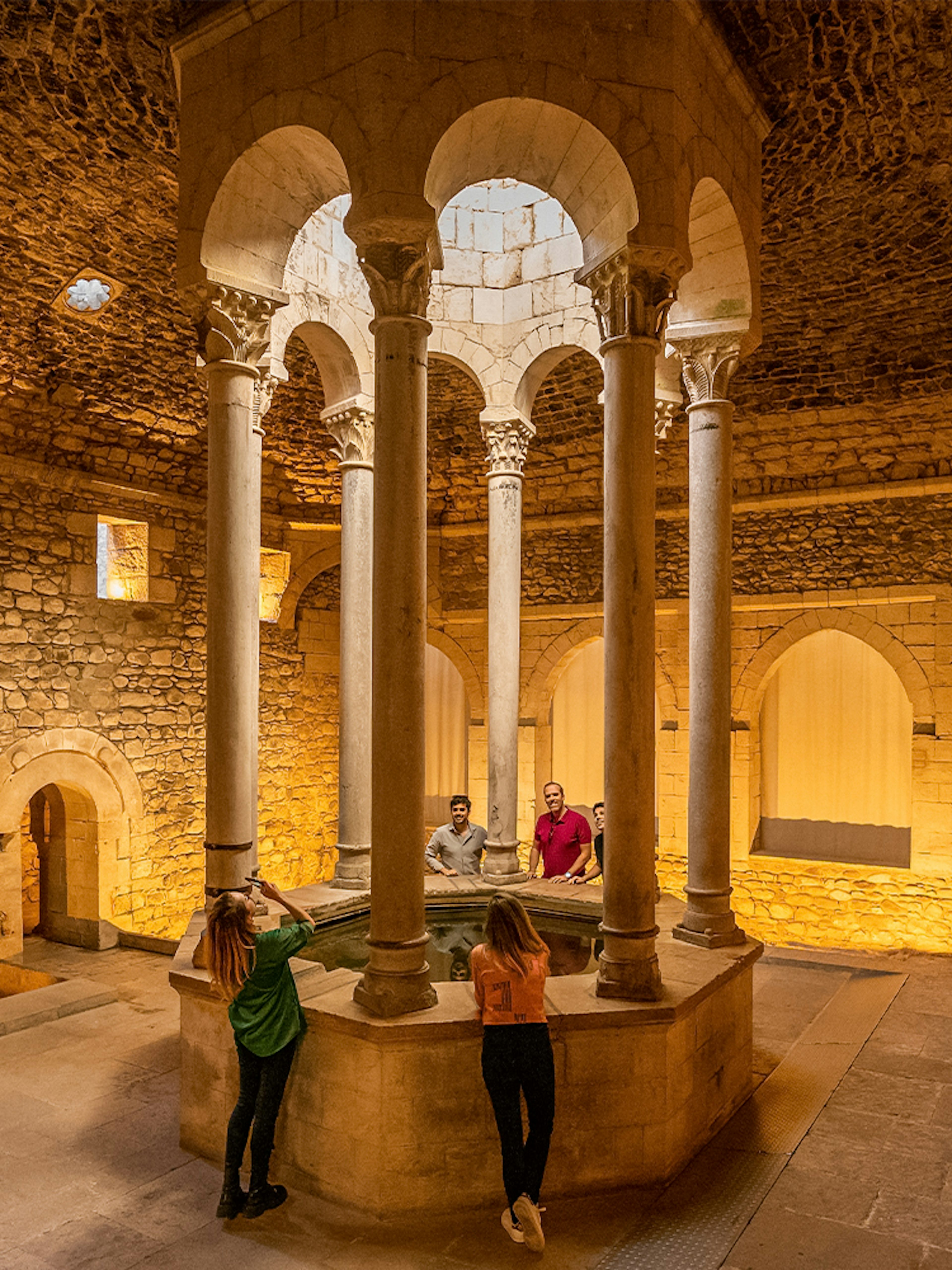 Tourists with guide in the Arab Baths of Girona, standing around central columns.