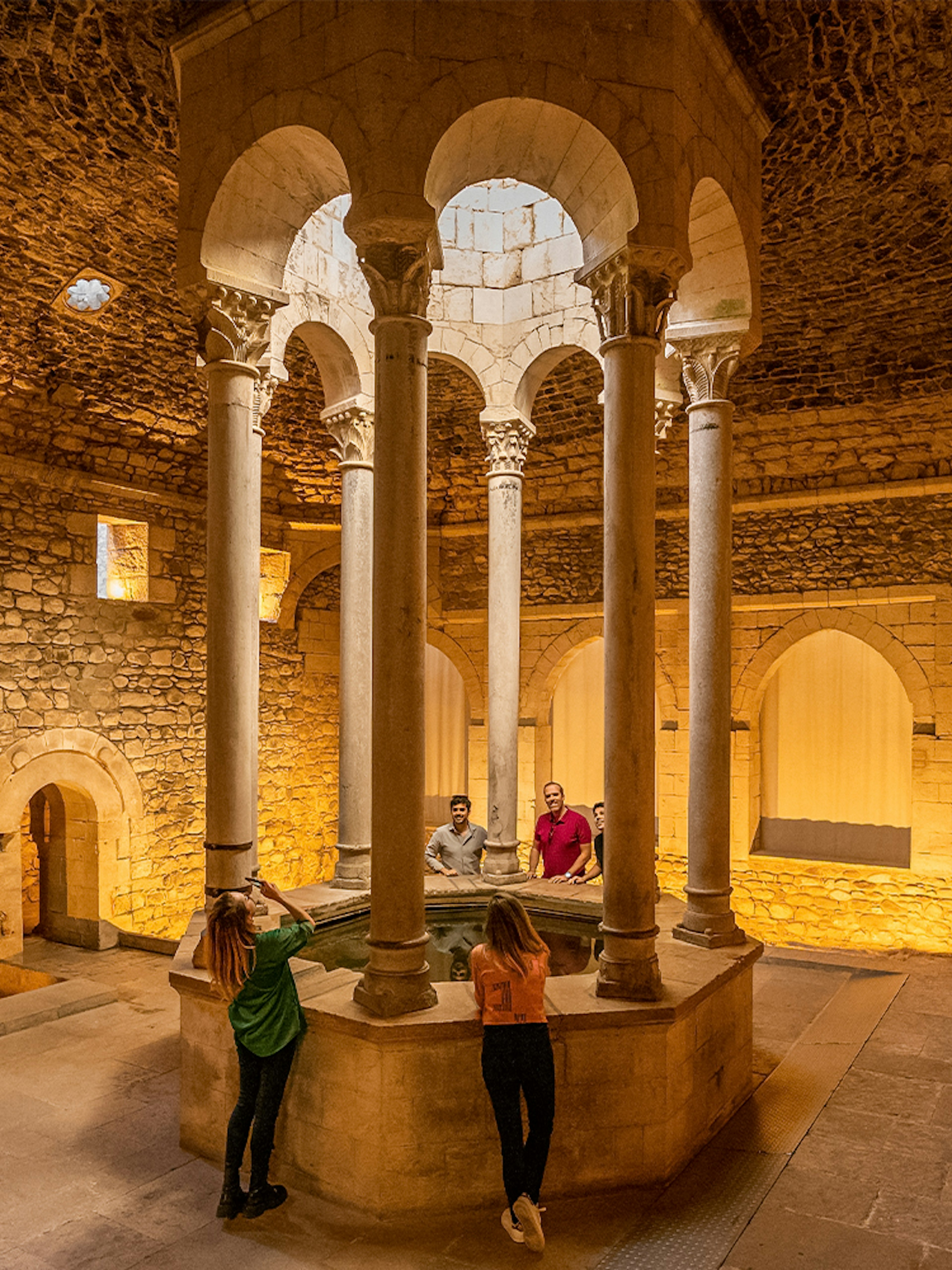 Tourists with guide in the Arab Baths of Girona, standing around central columns.