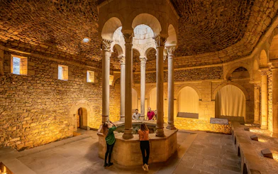 Tourists with guide in the Arab Baths of Girona, standing around central columns.