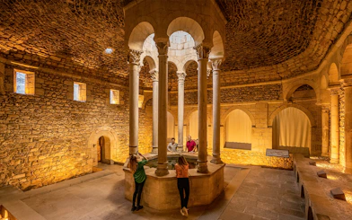 Tourists with guide in the Arab Baths of Girona, standing around central columns.