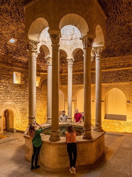 Tourists with guide in the Arab Baths of Girona, standing around central columns.