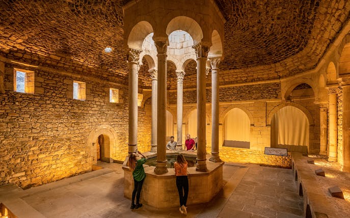 Tourists with guide in the Arab Baths of Girona, standing around central columns.