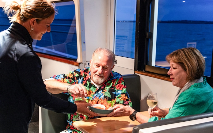 Server offering seafood dish to couple on Phillip Island sunset cruise.