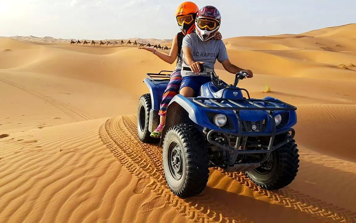 Quad biking on sand dunes during Dubai Desert Safari with camels in the background.