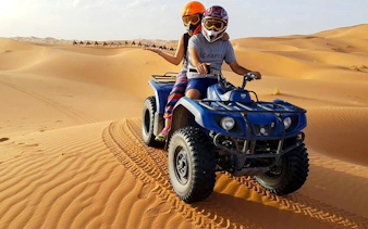 Quad biking on sand dunes during Dubai Desert Safari with camels in the background.