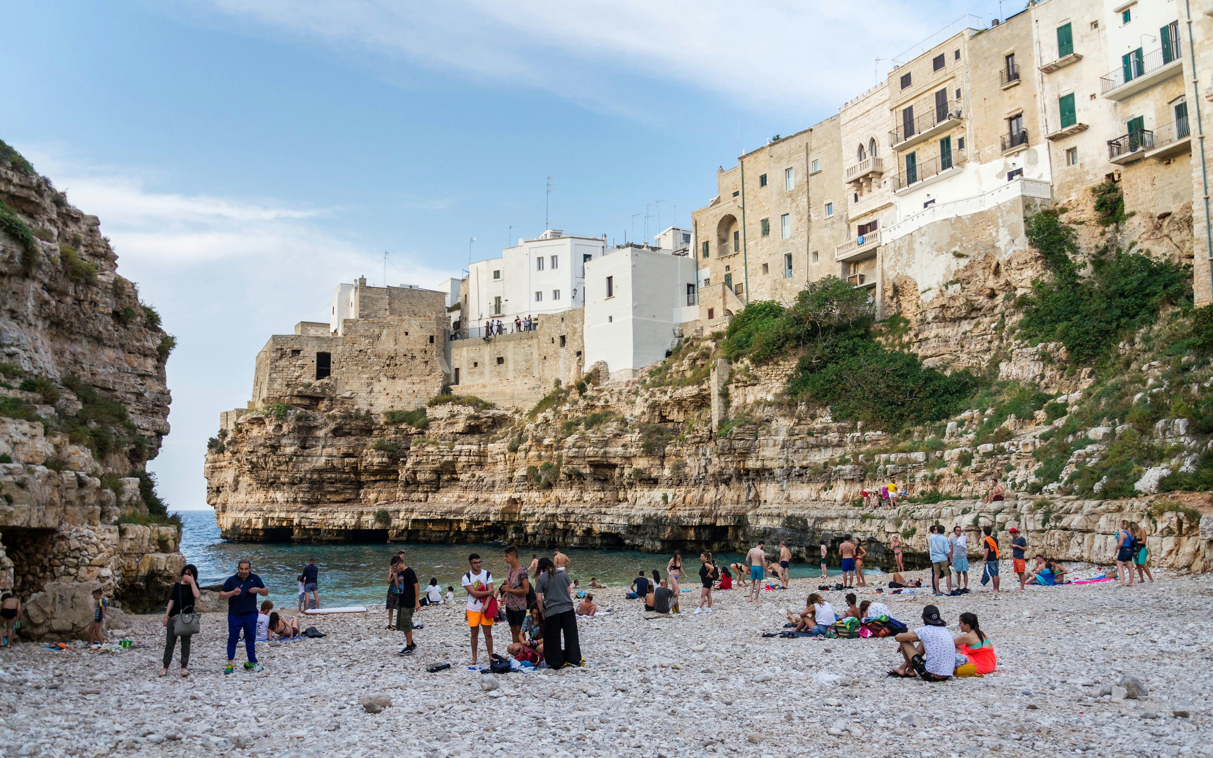 People enjoying Lama Monachile beach, surrounded by cliffs and historic buildings, Polignano a Mare, Italy.